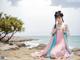 A woman in a pink and blue dress sitting on a beach.