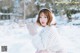 A woman in a white sweater and mittens sitting in the snow.