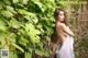 A woman in a white dress standing in front of a bush.